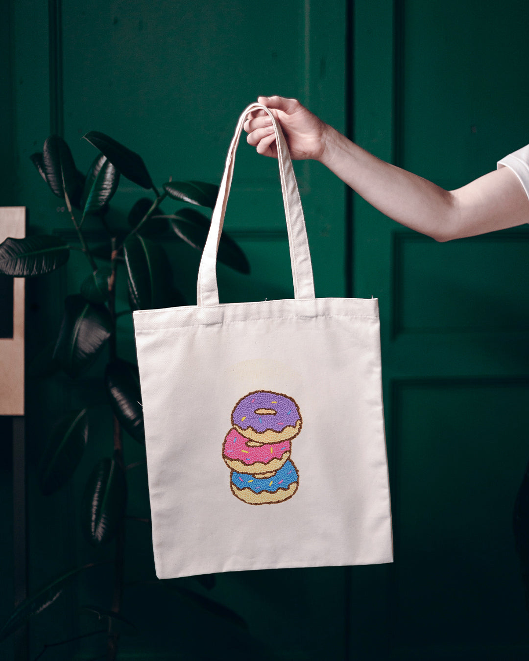 Tote bag with colorful donut design held by a person against a green background