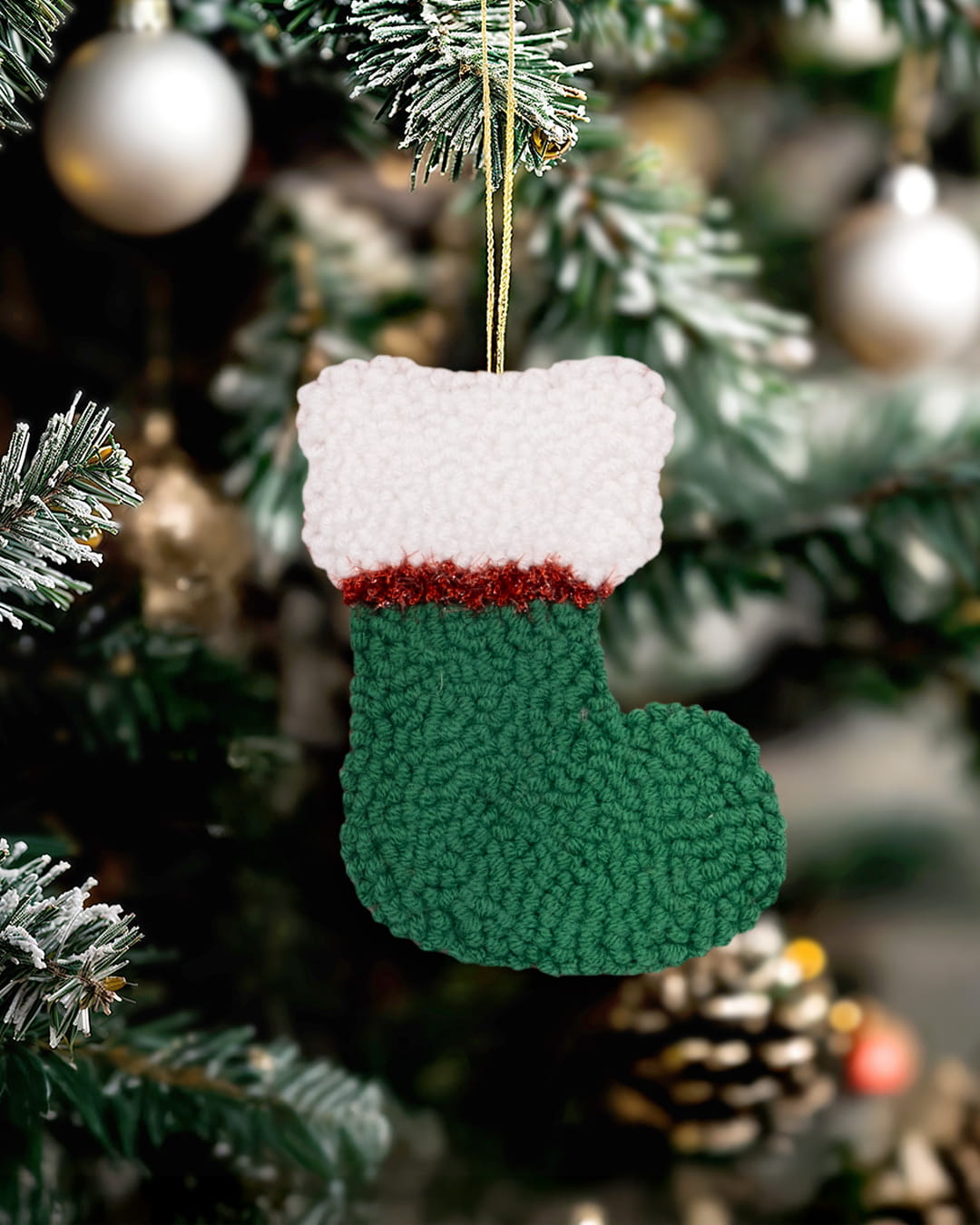 Handmade punch needle Christmas stocking ornament in green hanging on a decorated Christmas tree.