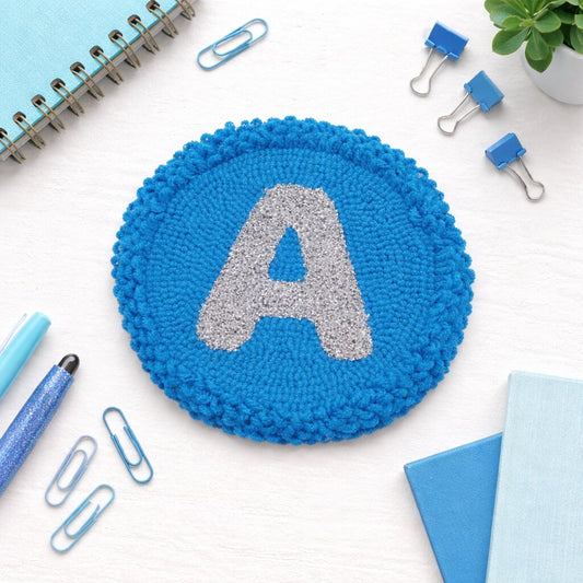 Alphabet A letter punch needle coaster styled on a table with coffee