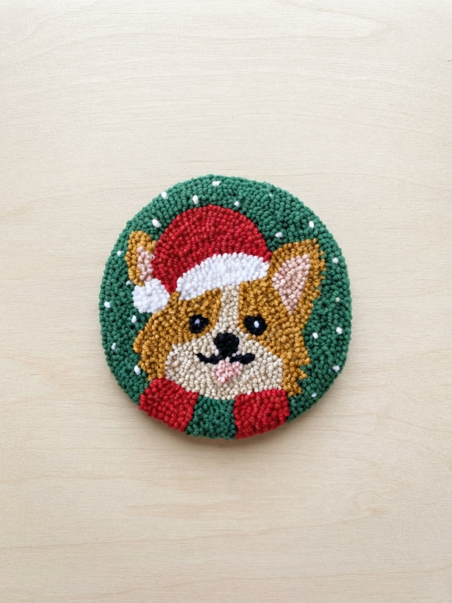 A circular hand-tufted rug featuring a corgi dog wearing a red Santa hat and scarf, set against a green background with white snowflake details, displayed on a light wood surface.