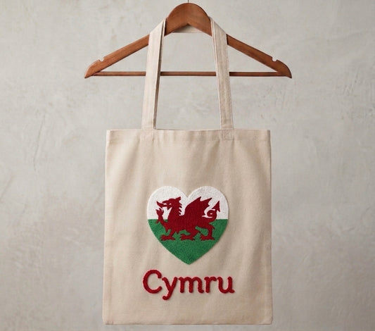 Welsh dragon tote bag with handmade punch needle heart flag design and Cymru lettering, hanging on a wooden hanger