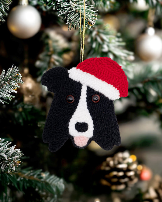 Handmade punch needle dog ornament wearing a Santa hat hanging on a Christmas tree.