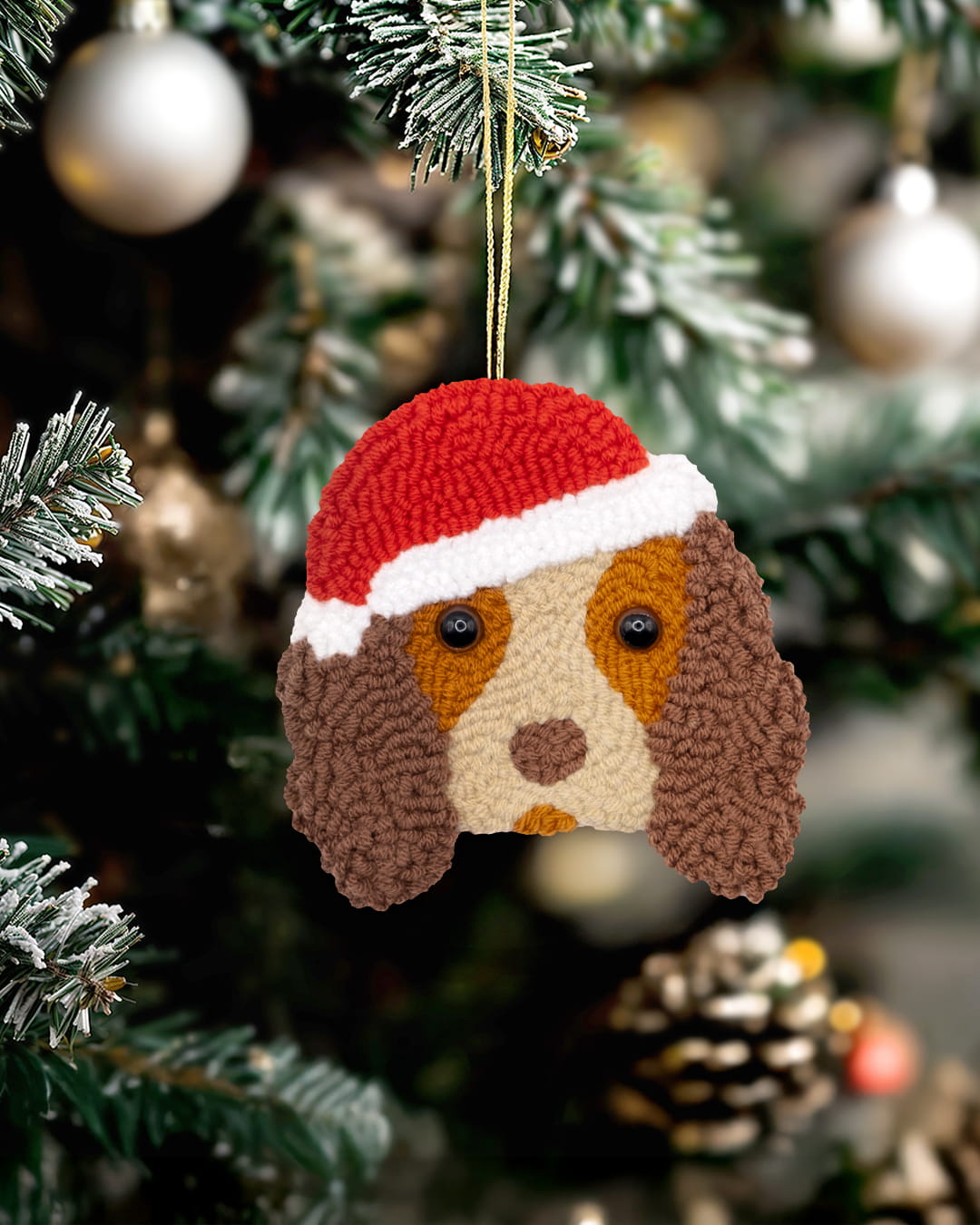 Handmade punch needle Cocker Spaniel ornament wearing a Santa hat hanging on a Christmas tree.