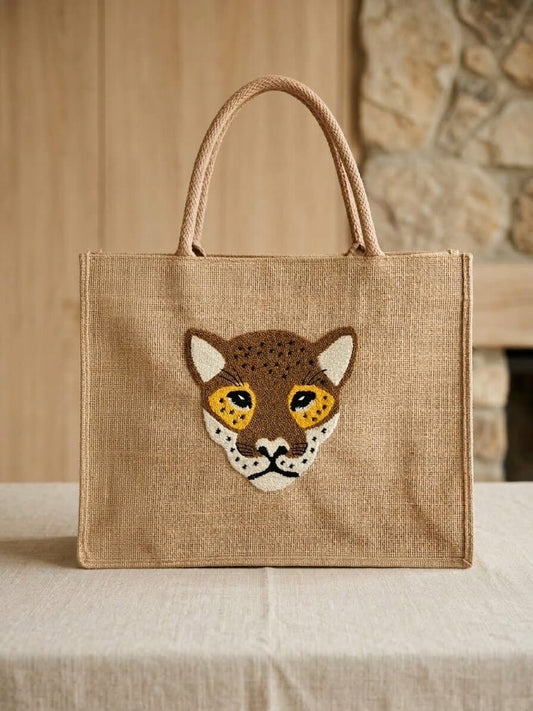Handmade jute shoulder bag with punch needle leopard face design placed on a table in a warm indoor setting.