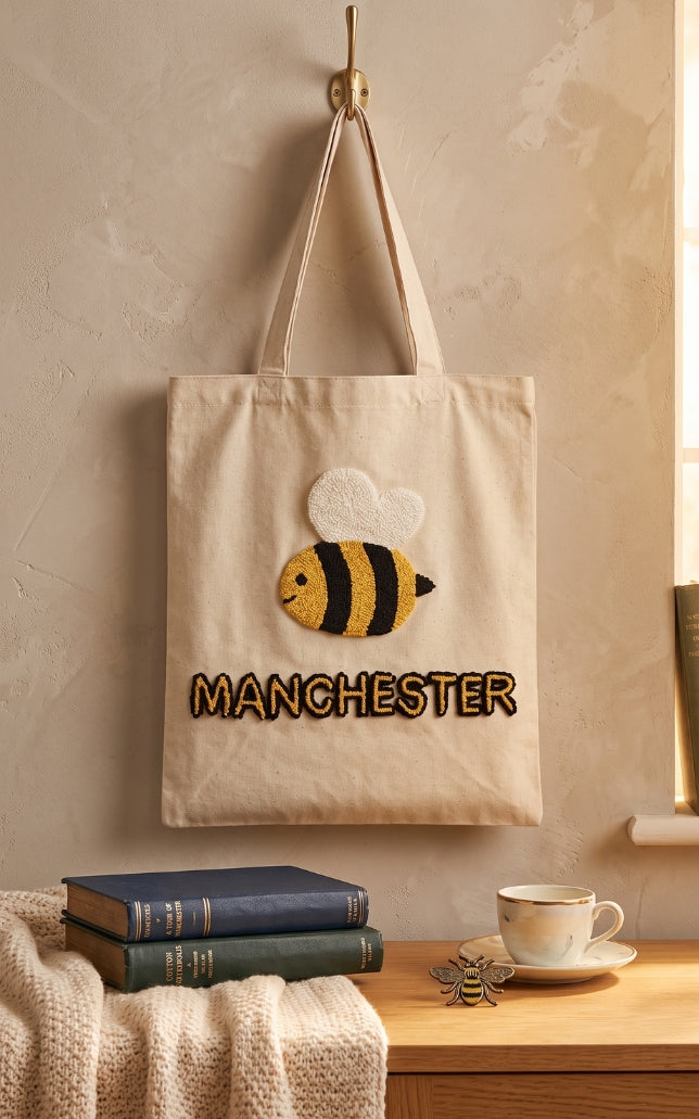 Manchester bee tote bag with handmade punch needle bee design and Manchester lettering, hanging on a hook
