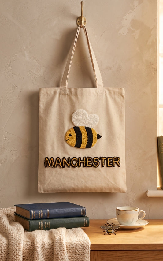 Manchester bee tote bag with handmade punch needle bee design and Manchester lettering, hanging on a hook