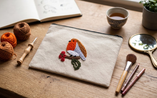 Robin bird zip pouch with handmade punch needle embroidery of a robin on a berry branch, laid on a wooden table