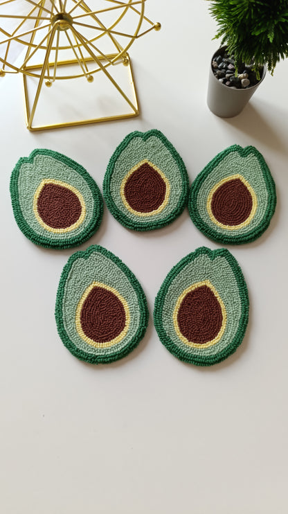 Five avocado half-shaped coasters arranged on a white surface, with a gold geometric decor object and a small potted plant in the background.