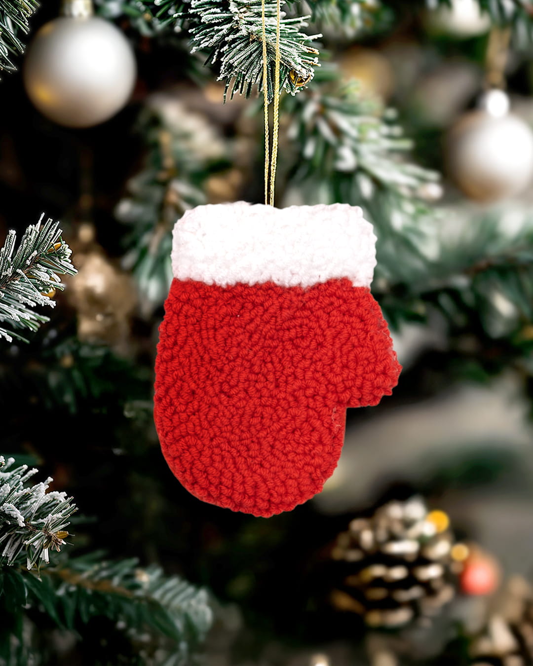 Handmade punch needle red mitten ornament with white cuff hanging on a decorated Christmas tree.