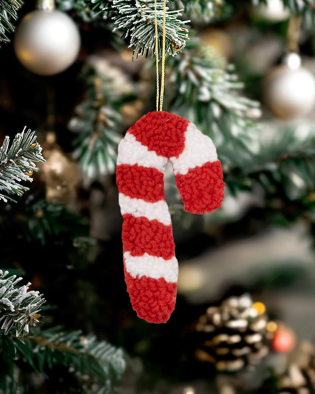 Handmade punch needle candy cane ornament in red and white hanging on a Christmas tree.