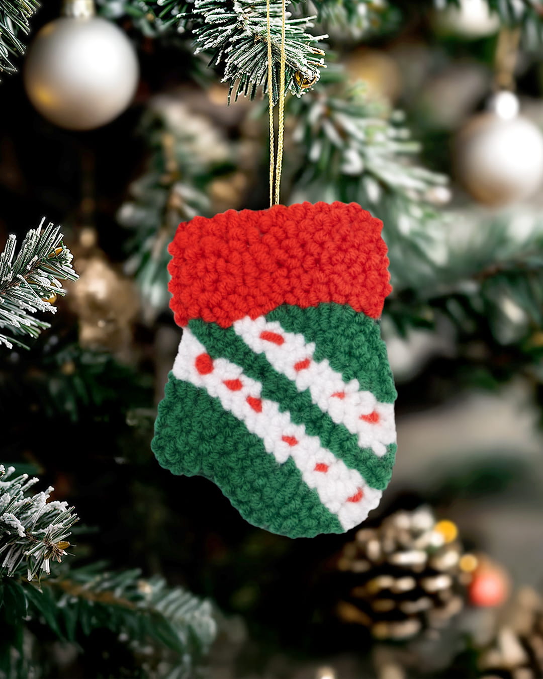 Handmade punch needle Christmas stocking ornament hanging on a decorated Christmas tree.- mitten