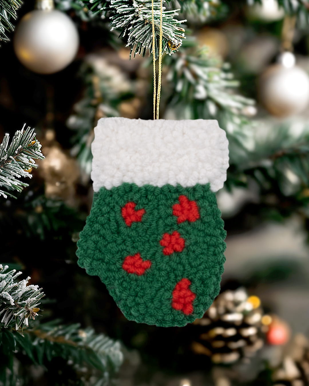 Handmade punch needle holly mitten ornament hanging on a decorated Christmas tree.