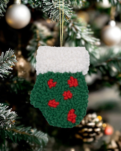 Handmade punch needle holly mitten ornament hanging on a decorated Christmas tree.