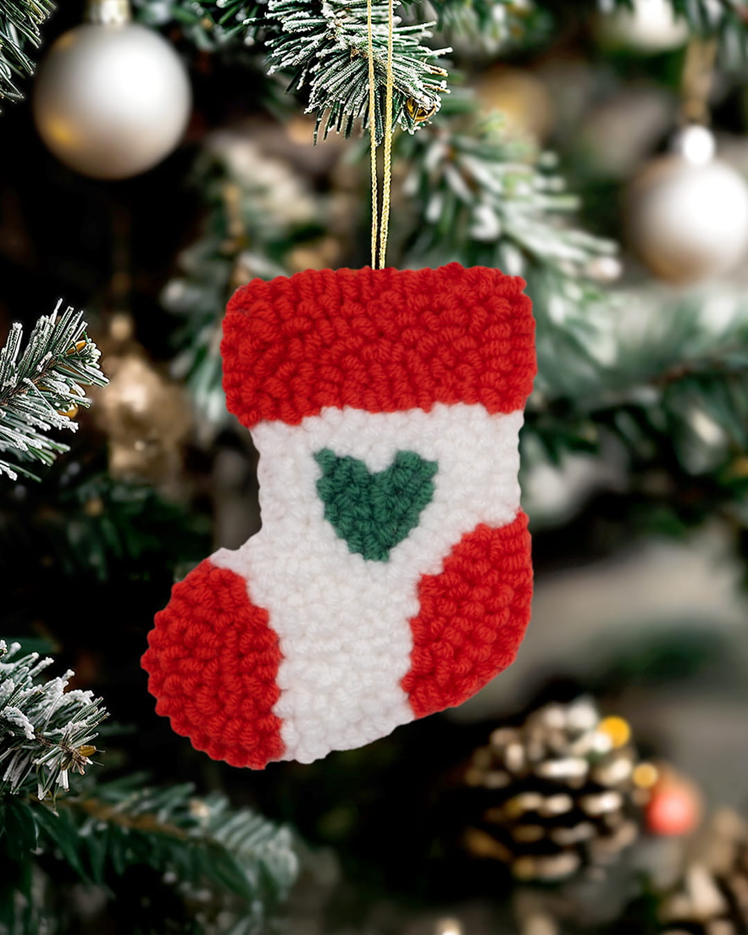 Handmade punch needle stocking ornament with green heart design hanging on a Christmas tree.