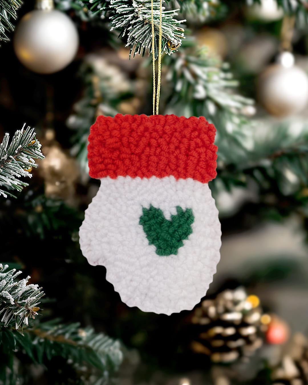 Handmade punch needle mitten ornament with green heart design hanging on a Christmas tree.