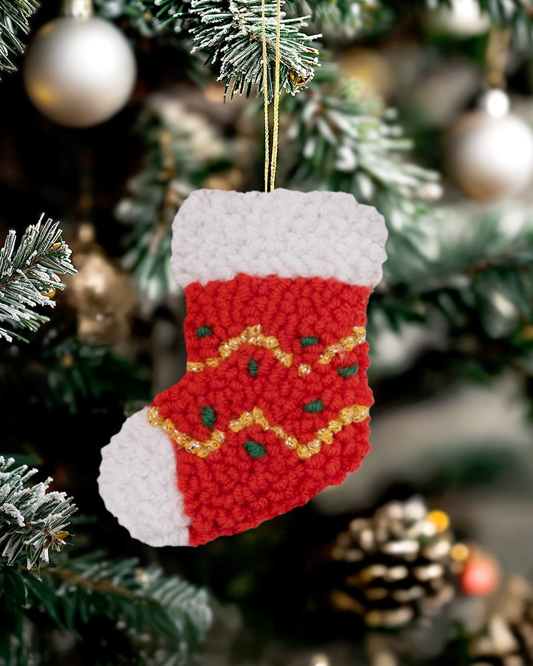 Handmade punch needle sparkle stocking ornament hanging on a decorated Christmas tree.