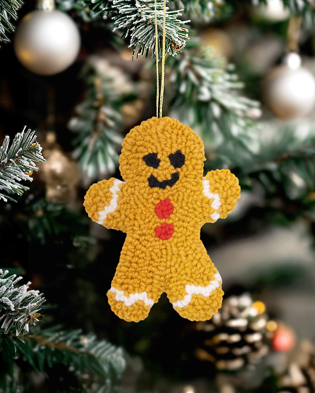 Handmade punch needle gingerbread ornament hanging on a Christmas tree.