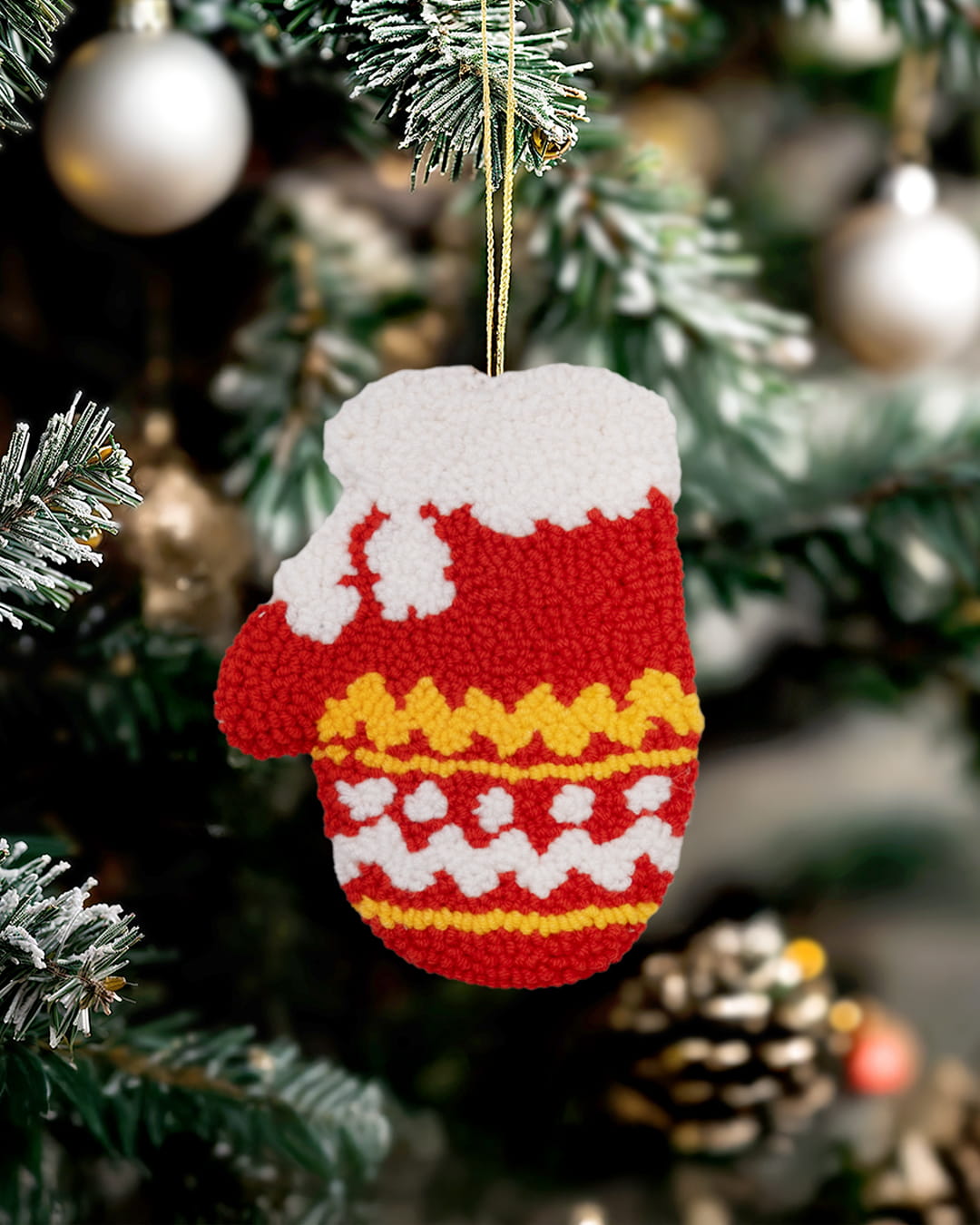 Handmade punch needle festive mitten ornament with red and white pattern hanging on a decorated Christmas tree.