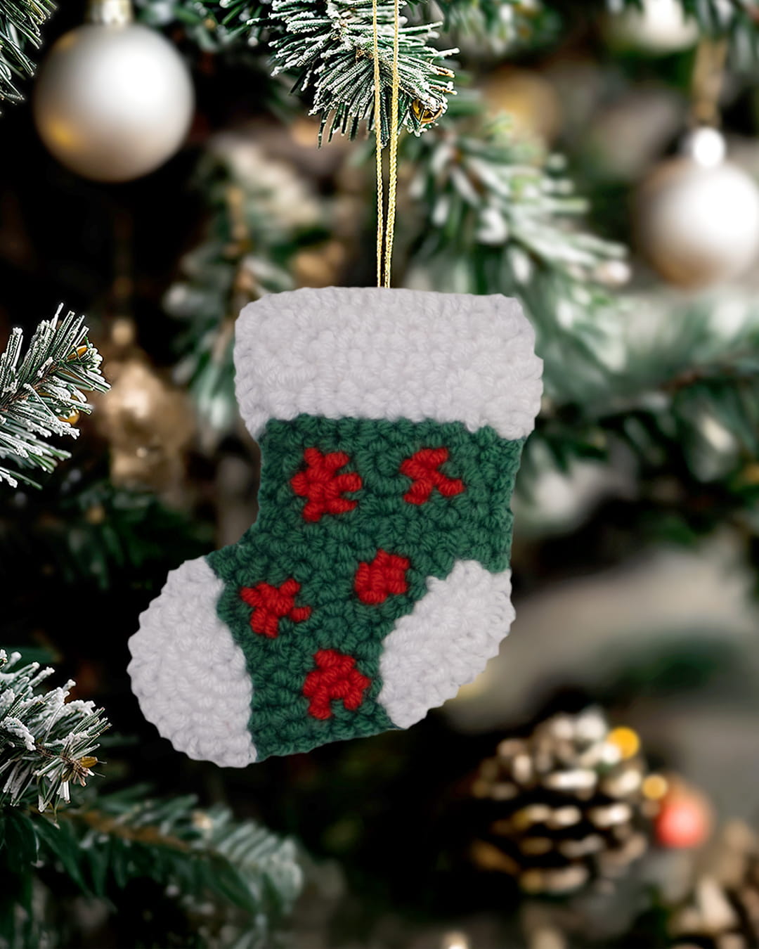 Handmade punch needle holly stocking ornament hanging on a decorated Christmas tree.
